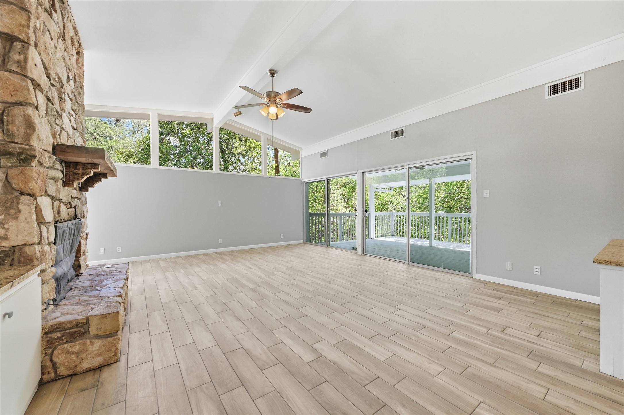 7 Hull Circle Austin, TX 78746 - Photo 3 of 14 Unfurnished living room with wood finish floors, a stone fireplace, ceiling fan, and vaulted ceiling