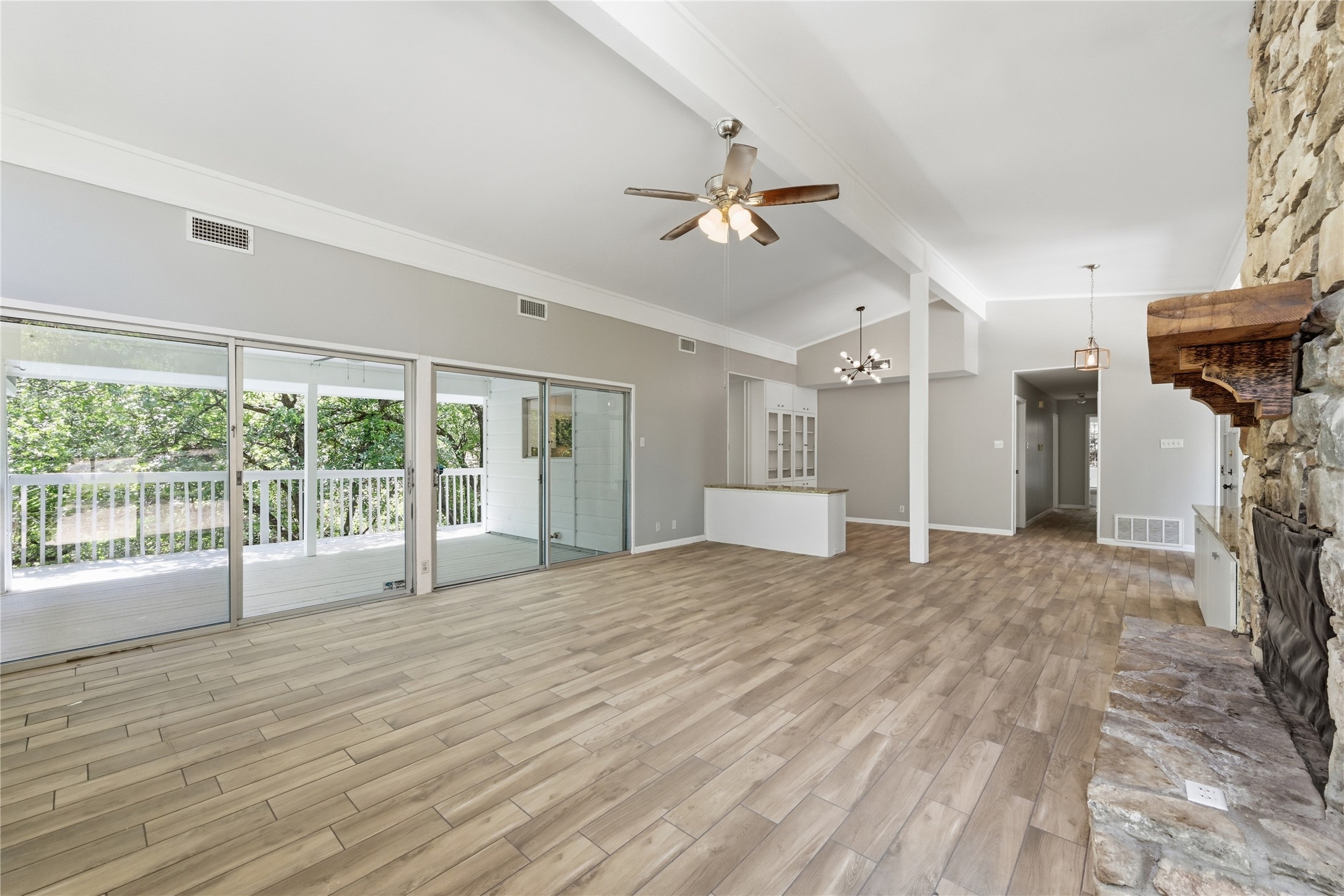 7 Hull Circle Austin, TX 78746 - Photo 4 of 14 Unfurnished living room with a ceiling fan, light wood-type flooring, lofted ceiling with beams, and hanging lights