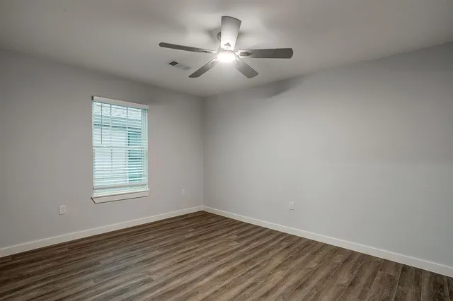 an empty room with wooden floor chandelier fan and windows