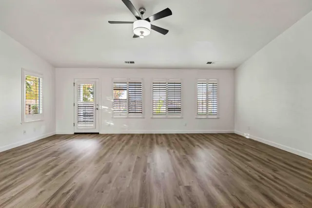 an empty room with wooden floor chandelier fan and windows