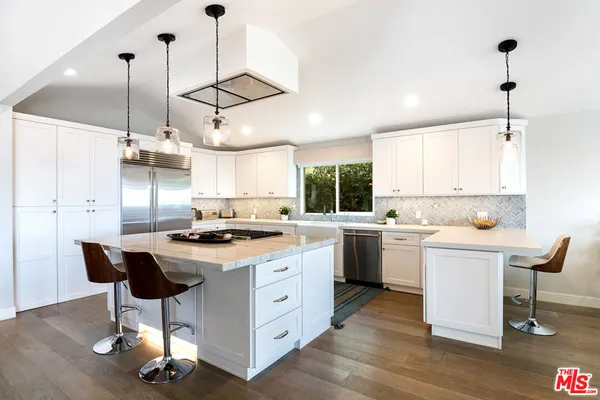 a kitchen with kitchen island a stove a dining table chairs and white cabinets