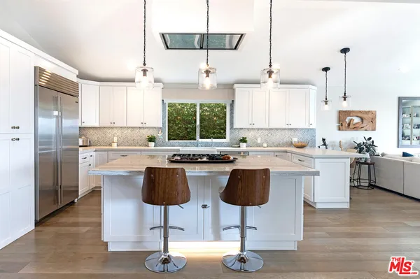 a kitchen with stainless steel appliances granite countertop a stove a sink a refrigerator and white cabinets with wooden floor