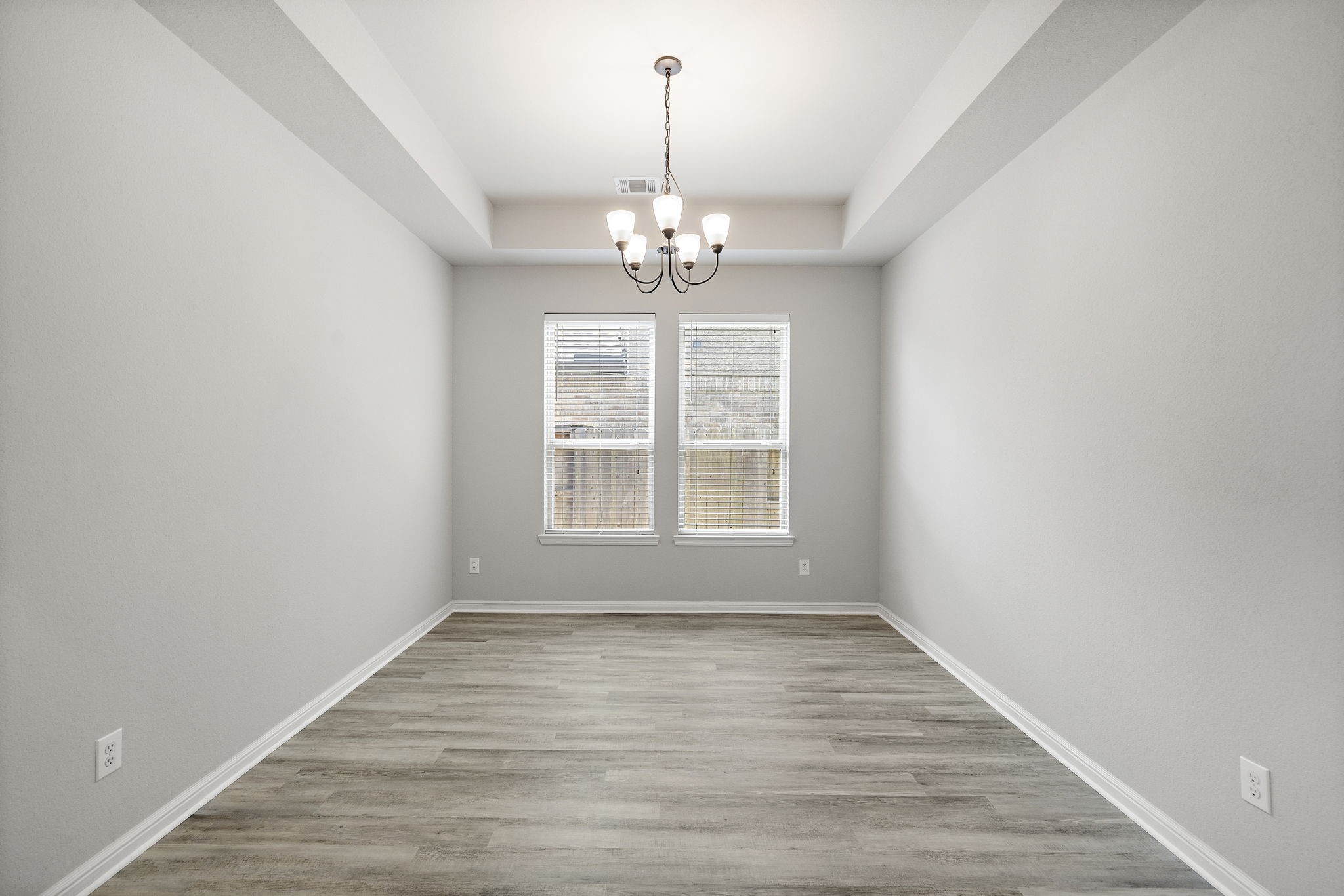 27924 Seger Bnd Trail Spring, TX 77386 - Photo 15 of 21 A well-lit dining room with light gray walls and wood-style flooring. A modern chandelier hangs from the ceiling, and two large windows provide natural light.