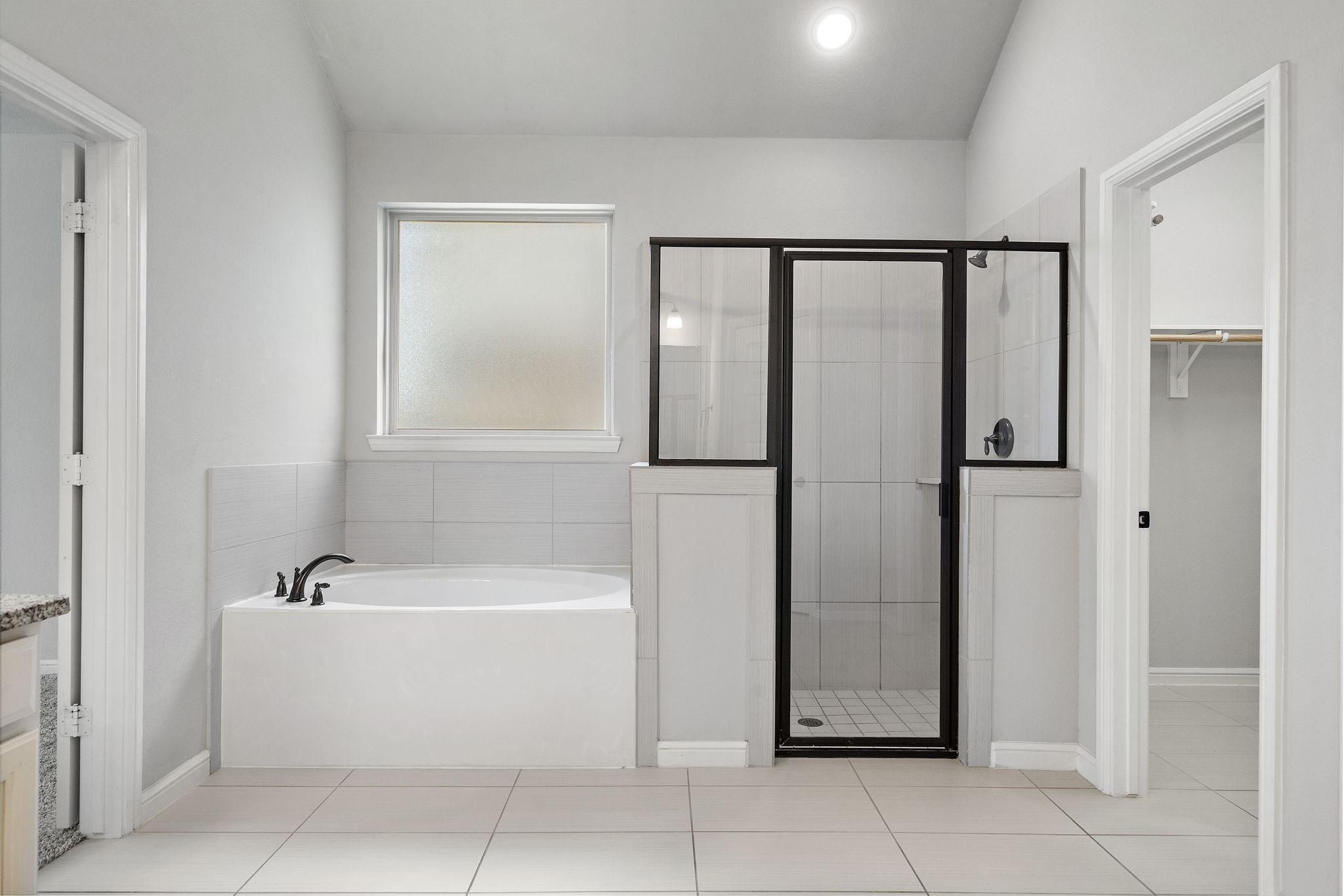 27924 Seger Bnd Trail Spring, TX 77386 - Photo 18 of 21 This bathroom features a modern design with a soaking tub, a separate glass-enclosed shower, and bright, neutral tiles. It includes a frosted window for privacy and ample natural light.