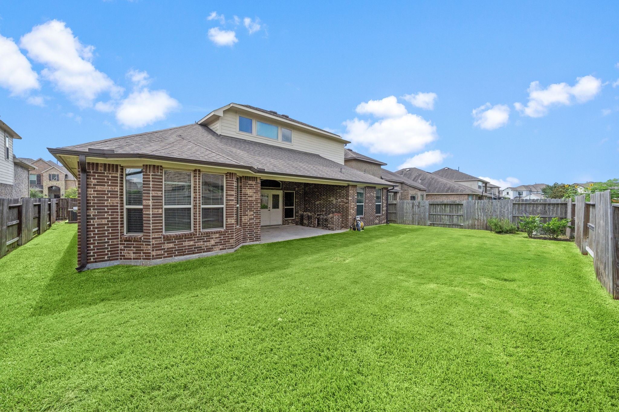 27924 Seger Bnd Trail Spring, TX 77386 - Photo 21 of 21 The backyard with a well-maintained lawn and a brick house featuring a covered patio. The area is fenced, providing privacy and a secure space for outdoor activities.