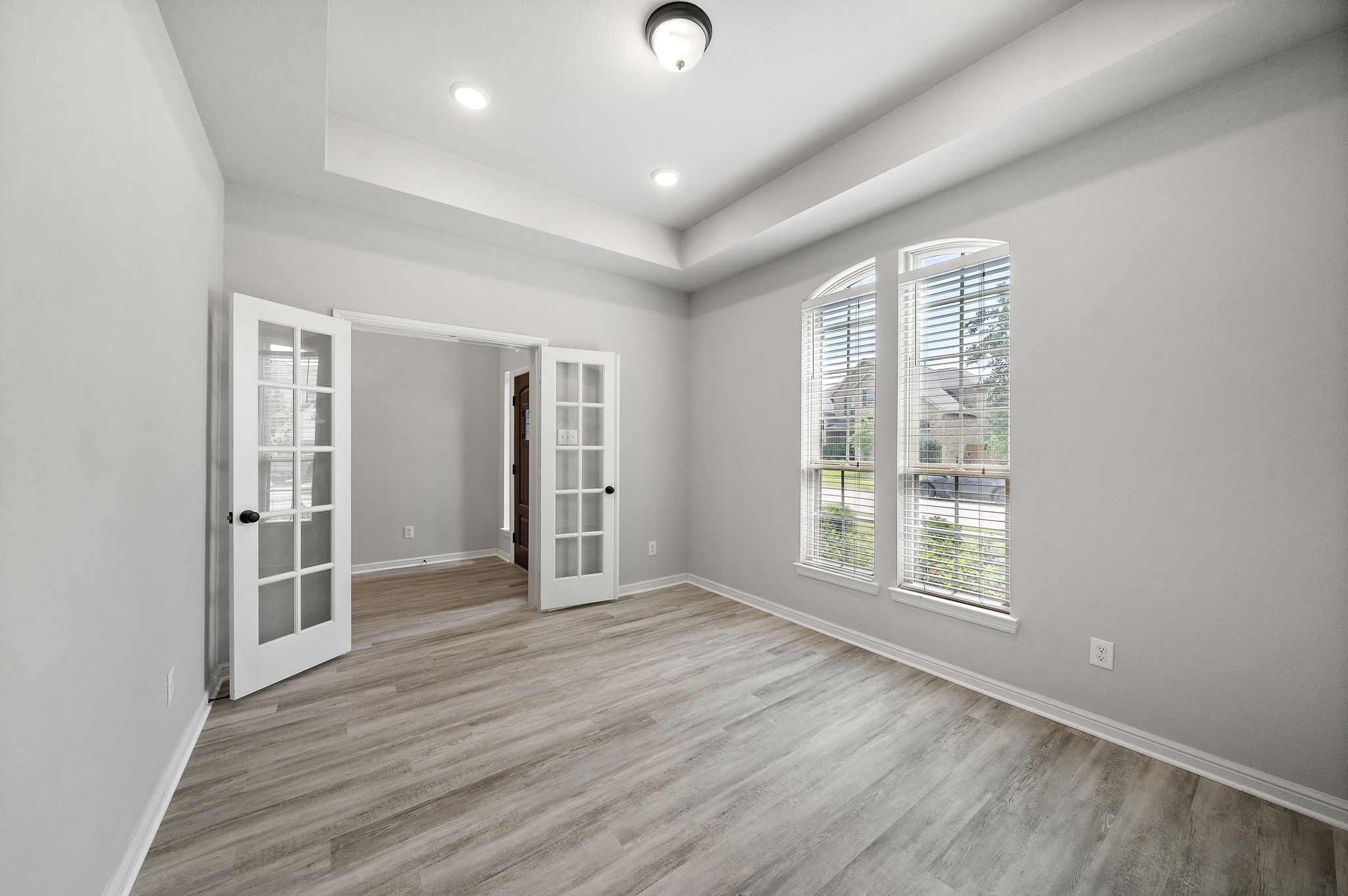 27924 Seger Bnd Trail Spring, TX 77386 - Photo 5 of 21 The office / study features elegant French doors, a tray ceiling, and large arched windows that fill the space with natural light. The neutral color palette and wood flooring create a modern and inviting atmosphere, perfect for a home office or study.