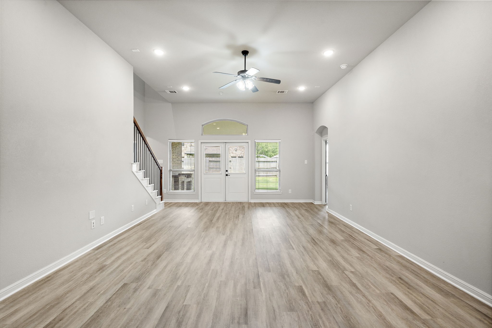 27924 Seger Bnd Trail Spring, TX 77386 - Photo 7 of 21 This spacious living area features high ceilings, sleek wood flooring, and ample natural light. It includes a ceiling fan and access to the backyard through double doors, with a staircase leading to the upper level.