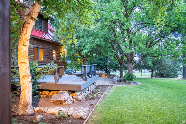 435 Canyon Road Millville, UT 84326 - Photo 54 of 113 Exterior featuring wood siding, a red metal roof, a composite deck, stone hardscaping, and mature trees