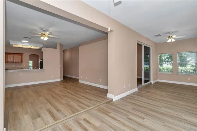 a view of an empty room with wooden floor and a kitchen