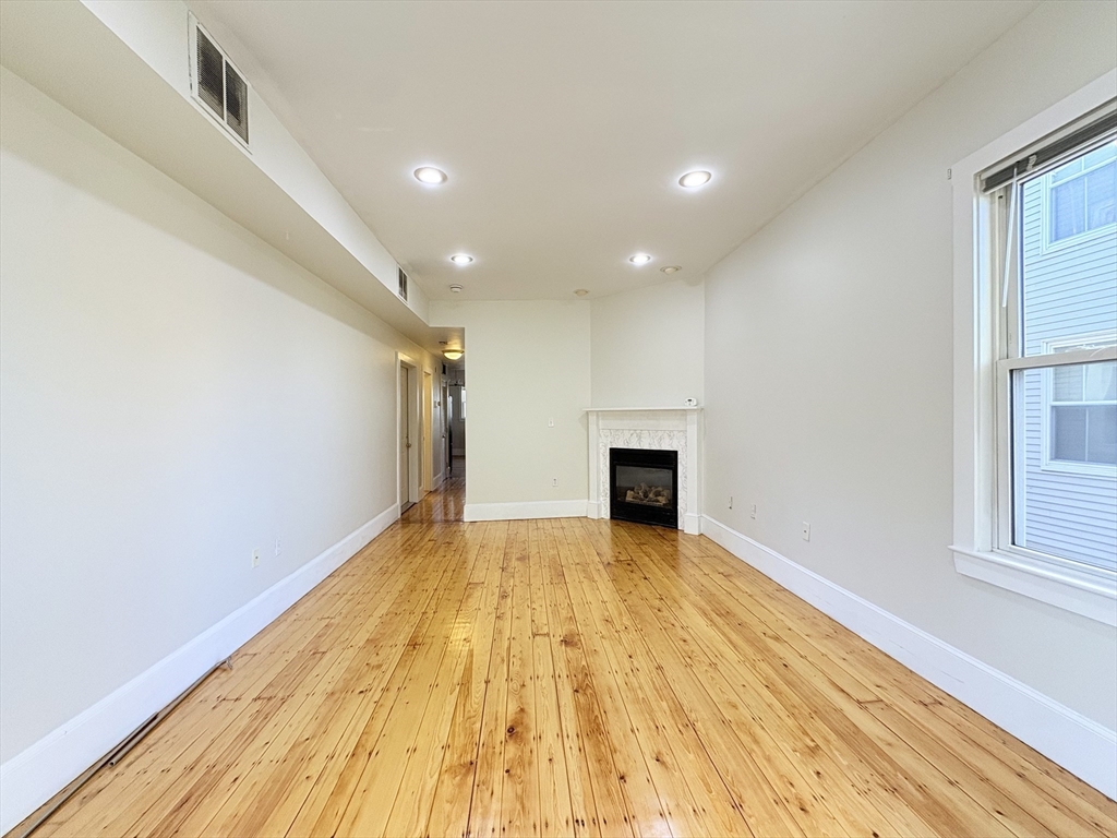 367 Cardinal Medeiros Avenue, Unit 1 Cambridge, MA 02141 - Photo 2 of 8 a view of empty room with wooden floor and fireplace