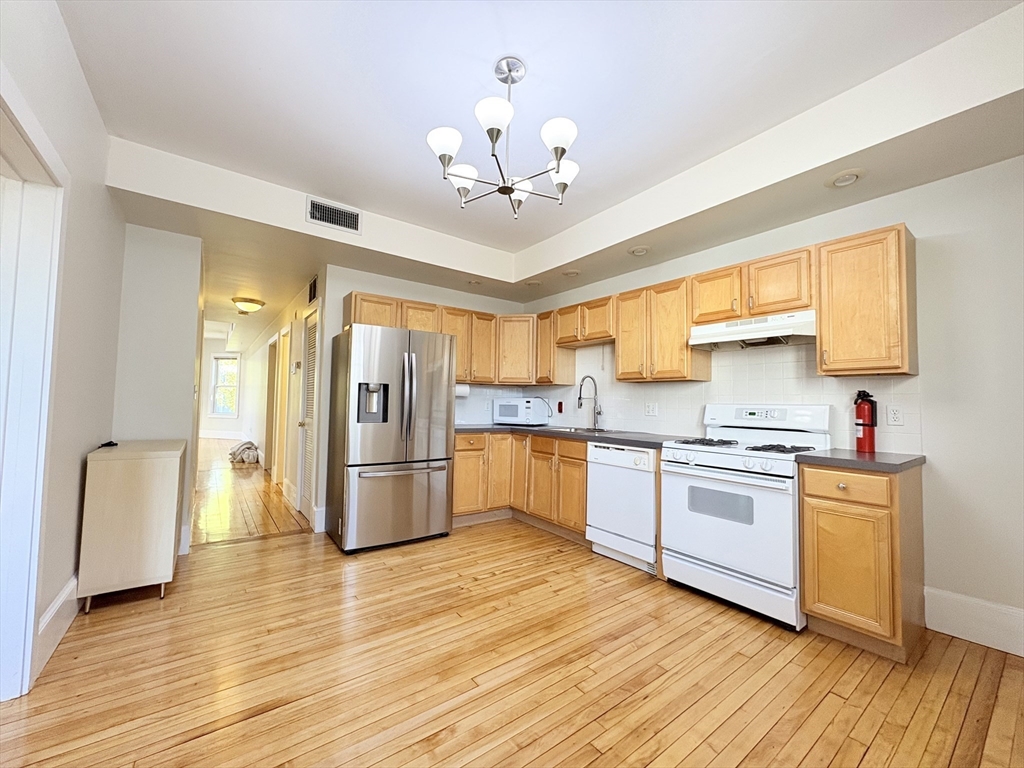 367 Cardinal Medeiros Avenue, Unit 1 Cambridge, MA 02141 - Photo 6 of 8 a kitchen with stainless steel appliances granite countertop a refrigerator a sink dishwasher a stove and white countertops with wooden floor