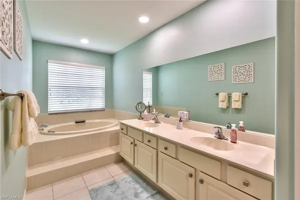 a spacious bathroom with a double vanity sink a large mirror a bathtub and next to a window
