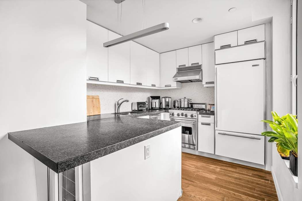 261 West 28th Street, Unit 9C Manhattan, NY 10001 - Photo 2 of 12 a kitchen with stainless steel appliances granite countertop a refrigerator a sink dishwasher a stove and white countertops with wooden floor