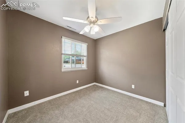 an empty room with a chandelier fan and windows