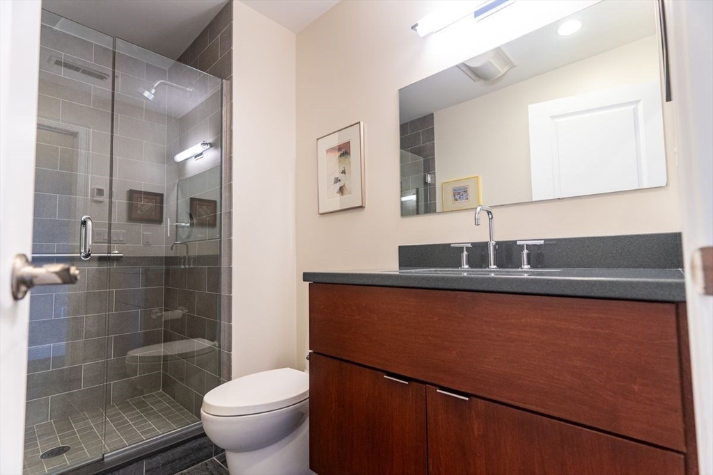 1 South Cottage Road, Unit 1 Belmont, MA 02478 - Photo 19 of 35 a bathroom with a granite countertop sink a toilet a mirror and shower