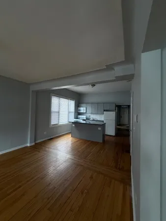 a view of empty room with wooden floor and kitchen
