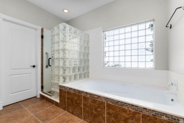 1417 Blacksmith Lane Draper, UT 84020 - Photo 17 of 57 Bathroom featuring a glass block shower enclosure, a white soaking tub with tiled surround, a large glass block window, and brown tile flooring