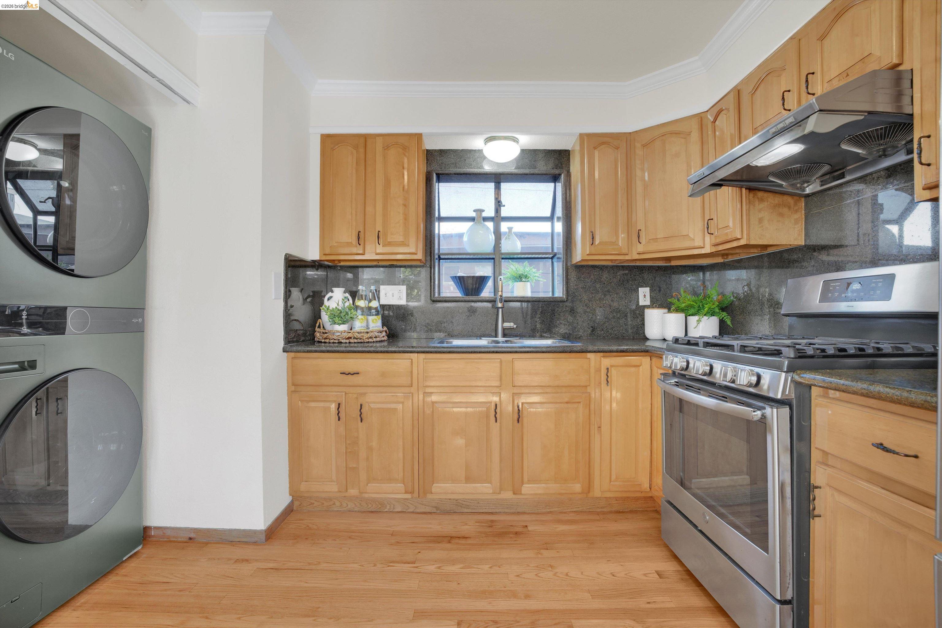 1821 Grand Street Alameda, CA 94501 - Photo 11 of 32 Kitchen with gas range, decorative backsplash, ventilation hood, stacked washing machine and dryer, and ornamental molding