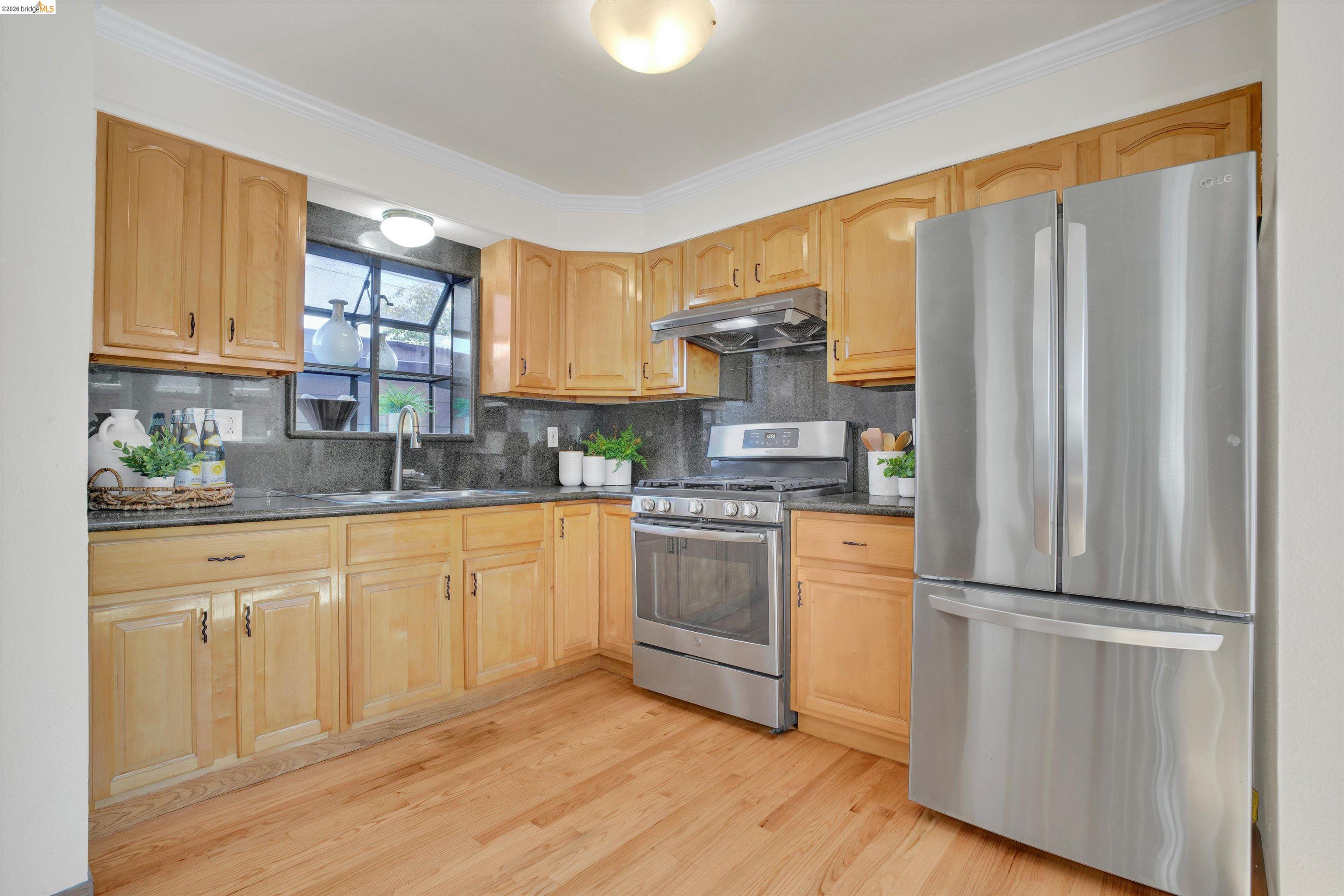 1821 Grand Street Alameda, CA 94501 - Photo 20 of 32 Kitchen featuring stainless steel appliances, dark stone countertops, backsplash, light wood-style flooring, and under cabinet range hood