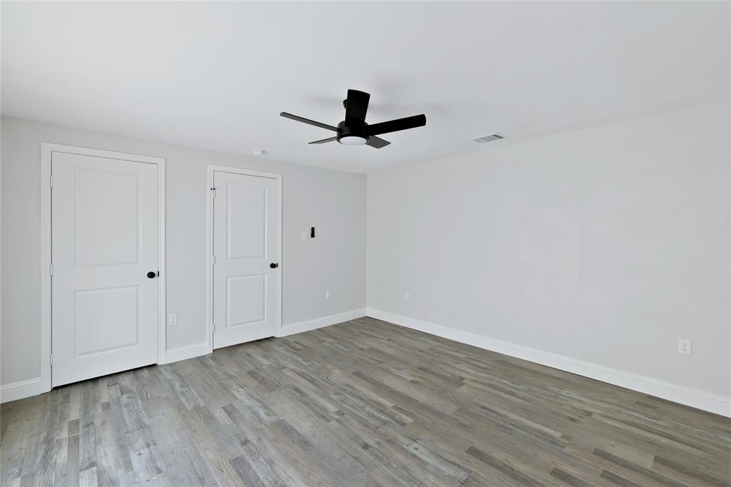 501 North Miller Street Decatur, TX 76234 - Photo 16 of 24 Wood-finish flooring, white walls, two paneled doors with black hardware, and a matte black ceiling fan with integrated lighting
