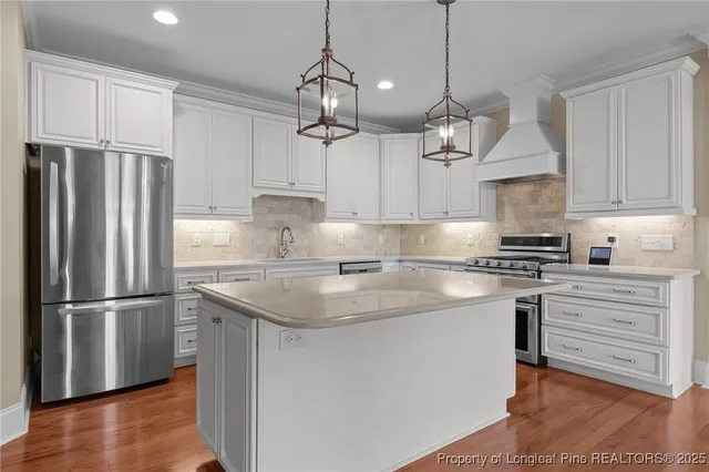 a kitchen with stainless steel appliances granite countertop a refrigerator a sink dishwasher a stove and white cabinets with wooden floor