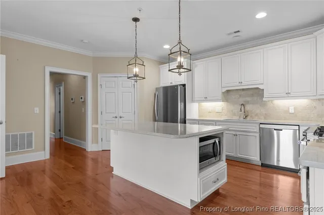 a kitchen with stainless steel appliances granite countertop a refrigerator a stove and white cabinets with wooden floor