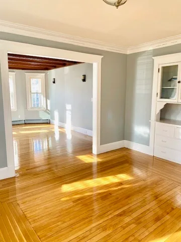 a view of empty room with wooden floor and kitchen view