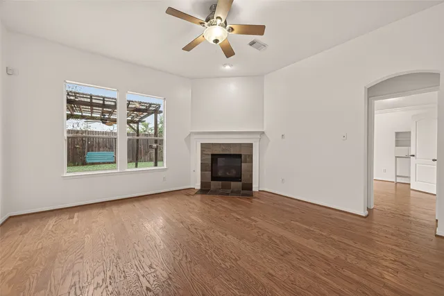 an empty room with wooden floor a ceiling fan and windows