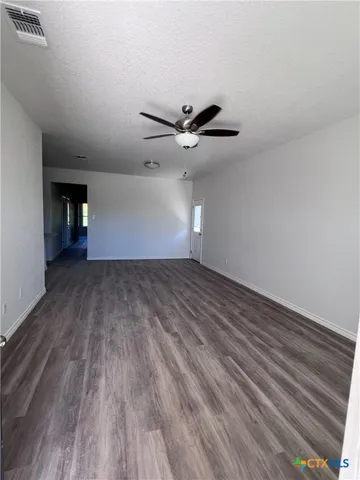 a view of an empty room with wooden floor and a ceiling fan