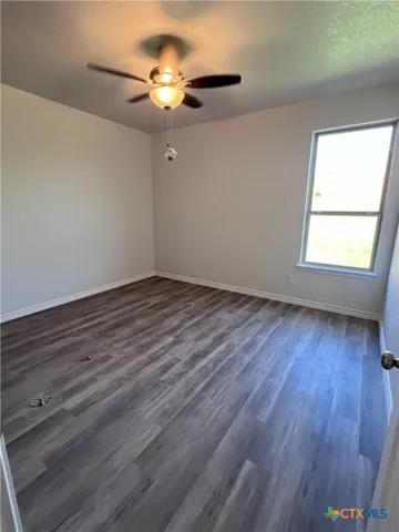 an empty room with wooden floor chandelier fan and windows