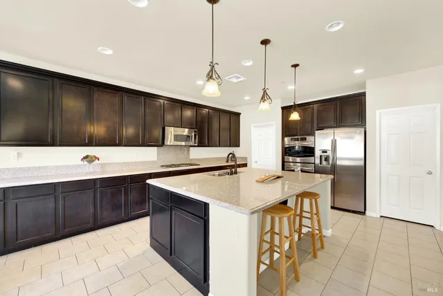 a kitchen with stainless steel appliances kitchen island granite countertop a table chairs sink and cabinets