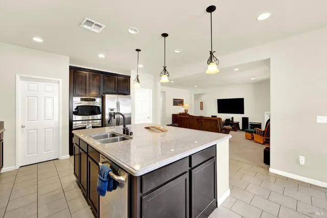 a kitchen with stainless steel appliances a sink a stove a refrigerator a center island and chairs
