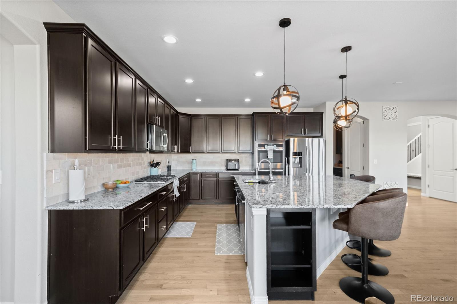 2910 El Nido Way Castle Rock, CO 80108 - Photo 12 of 50 a kitchen with stainless steel appliances kitchen island granite countertop a refrigerator a sink dishwasher a dining table and chairs with wooden floor