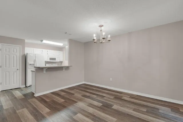a view of empty room with kitchen view and wooden floor