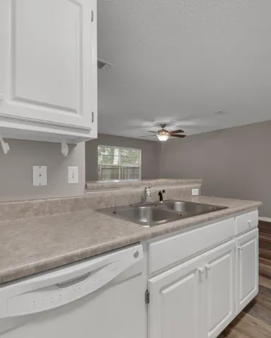 a view with granite countertop a sink and dishwasher with white cabinets