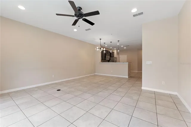 an empty room with chandelier fan and windows