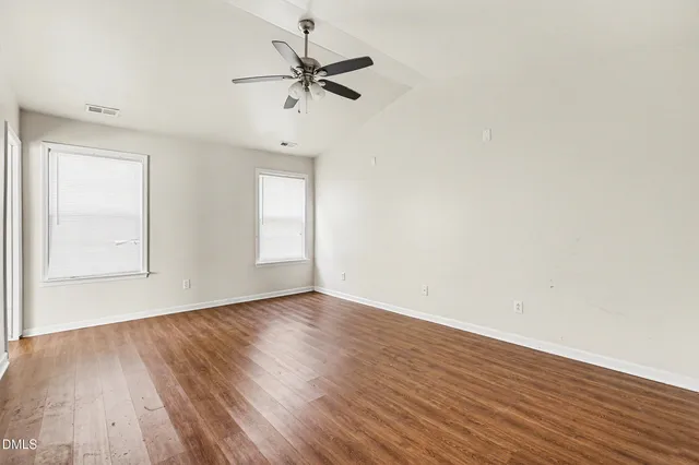 an empty room with wooden floor fan and windows