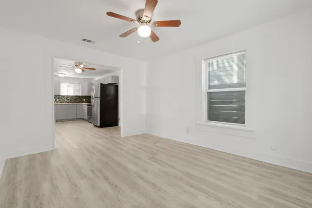 an empty room with wooden floor chandelier fan and windows
