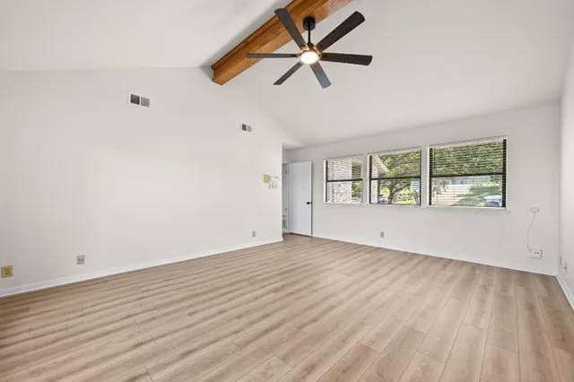 an empty room with wooden floor fan and windows