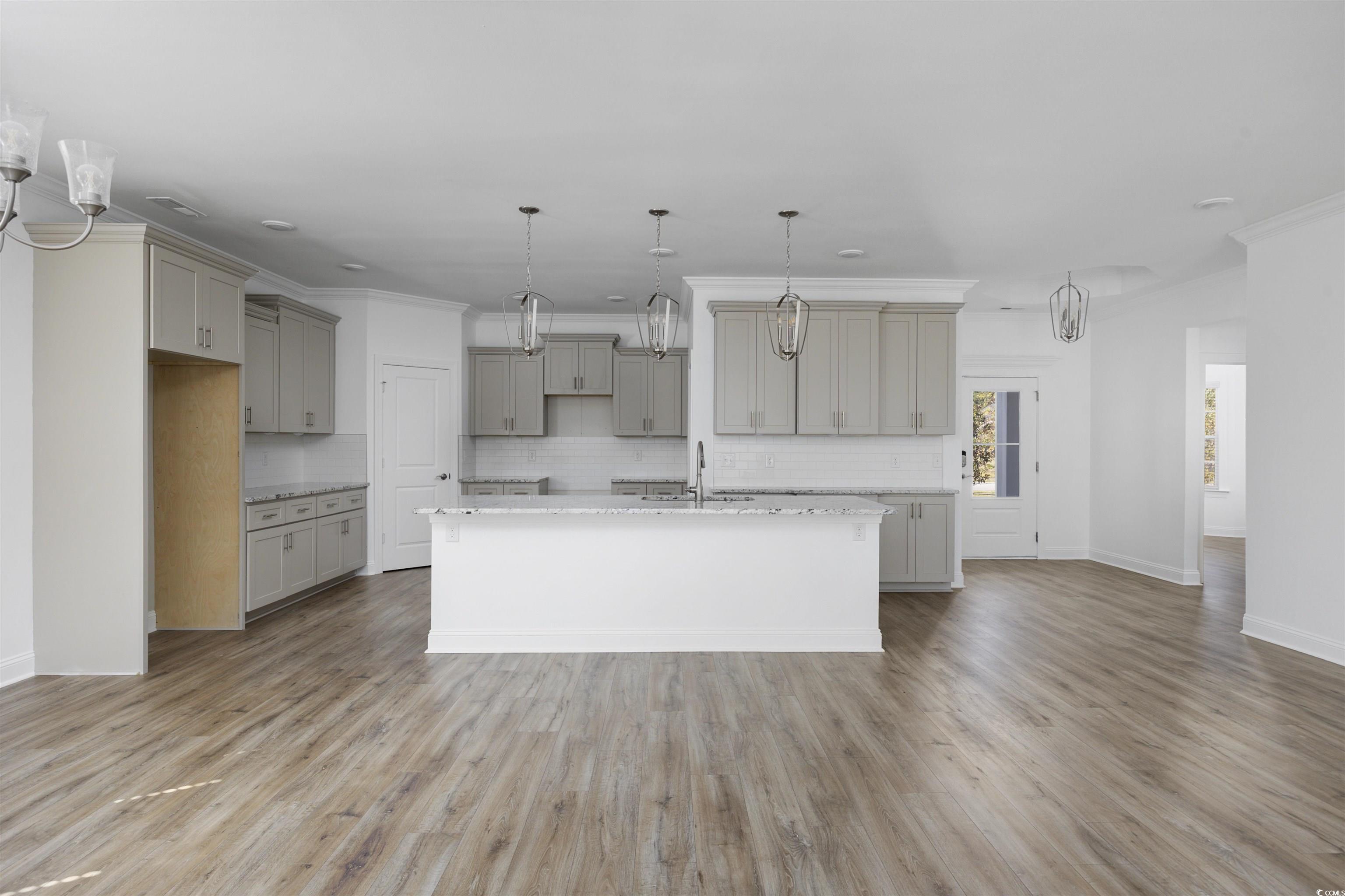 1108 Pochard Drive Conway, SC 29526 - Photo 13 of 37 Kitchen with gray cabinetry, decorative backsplash, an island with sink, light stone countertops, and light wood finished floors