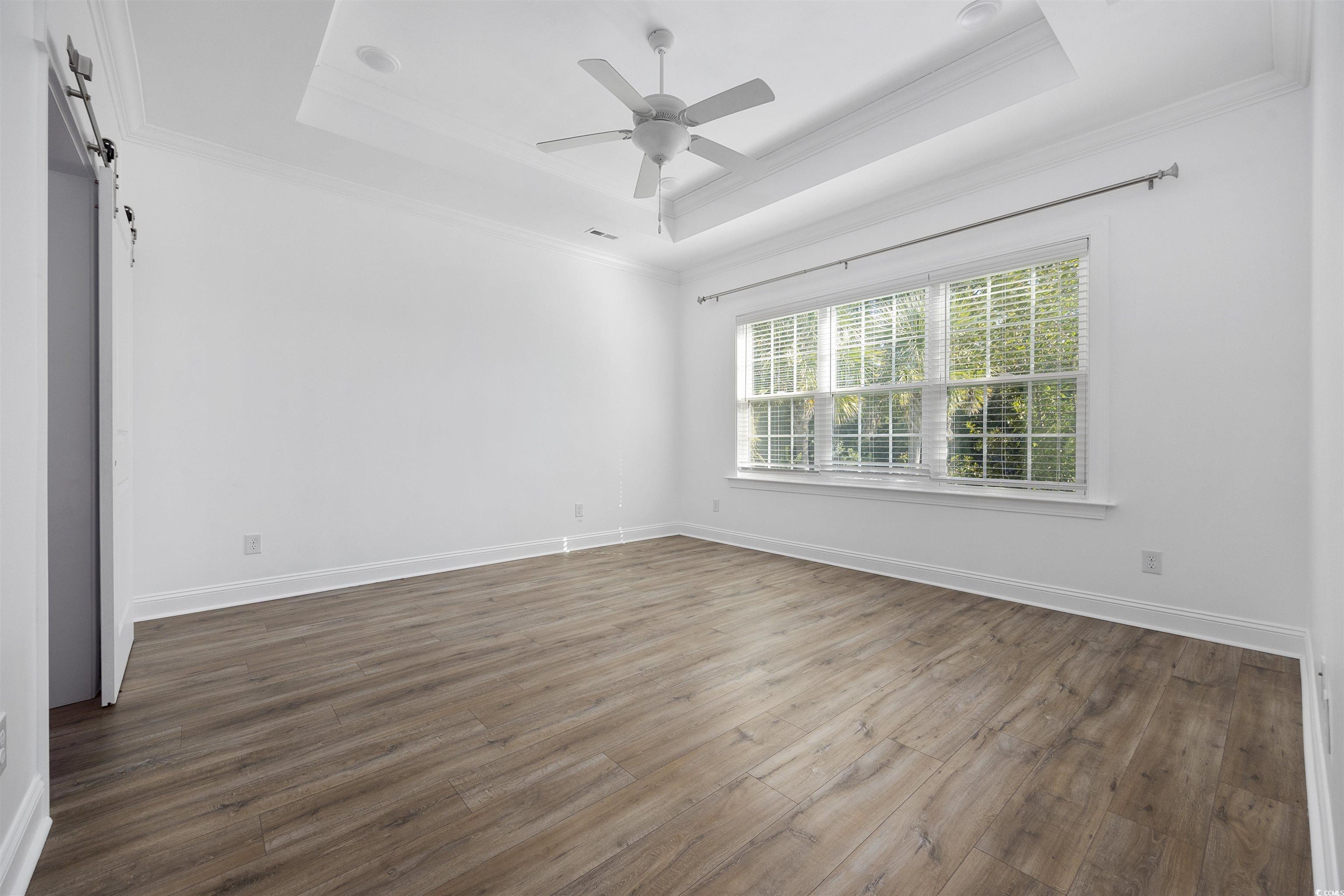 1108 Pochard Drive Conway, SC 29526 - Photo 17 of 37 Spare room featuring a tray ceiling, dark wood-style floors, a barn door, ornamental molding, and a ceiling fan