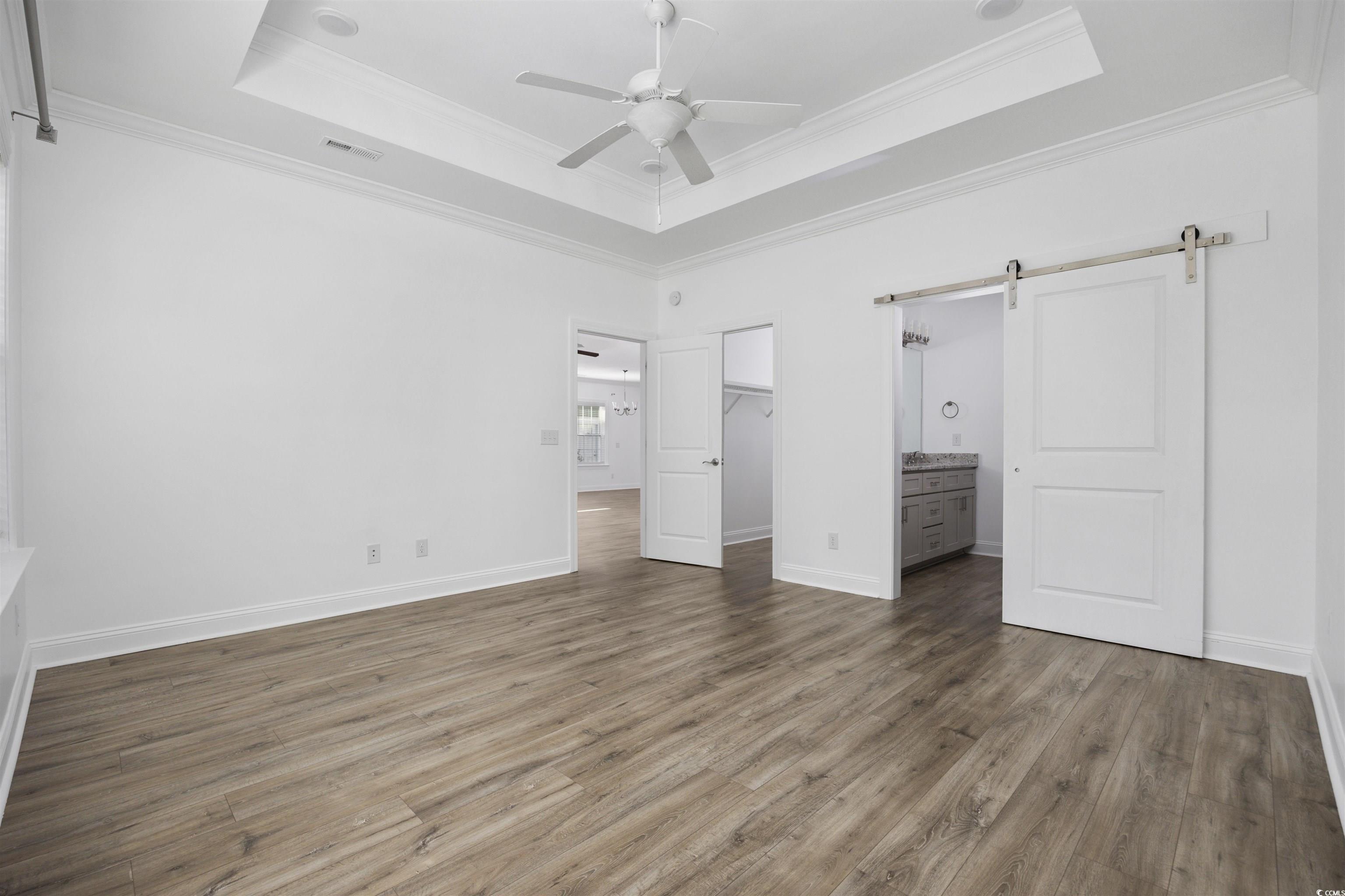 1108 Pochard Drive Conway, SC 29526 - Photo 20 of 37 Unfurnished bedroom with a barn door, a tray ceiling, dark wood finished floors, a spacious closet, and ornamental molding