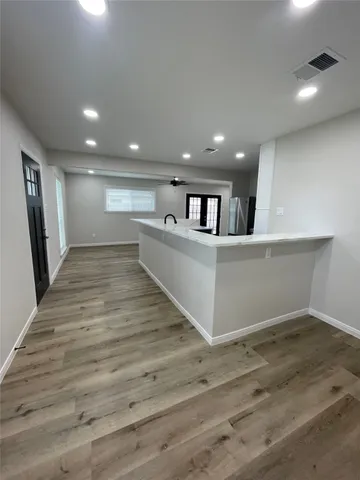 a view of an empty room with wooden floor and a kitchen