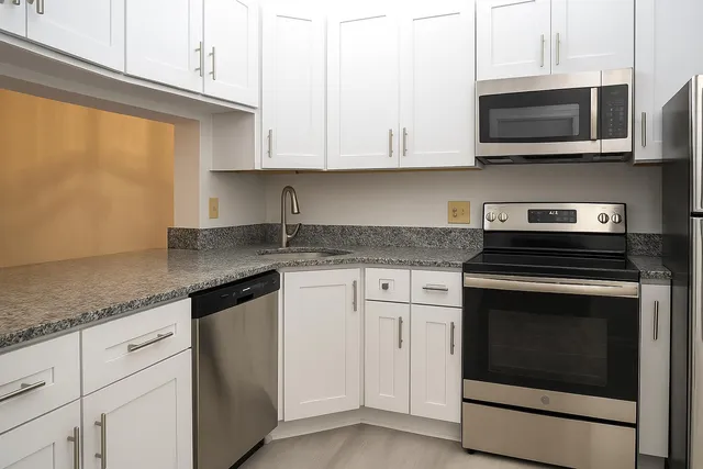a kitchen with granite countertop white cabinets stainless steel appliances and a counter space