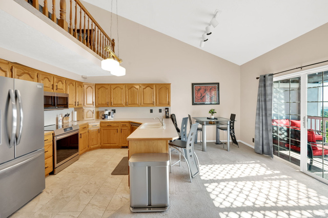 5057 South Ridgedale Drive Ogden, UT 84403 - Photo 24 of 69 Open-concept kitchen and dining area featuring light wood cabinetry, stainless steel appliances, tile flooring, a vaulted ceiling, and direct access to an outdoor deck through sliding glass doors
