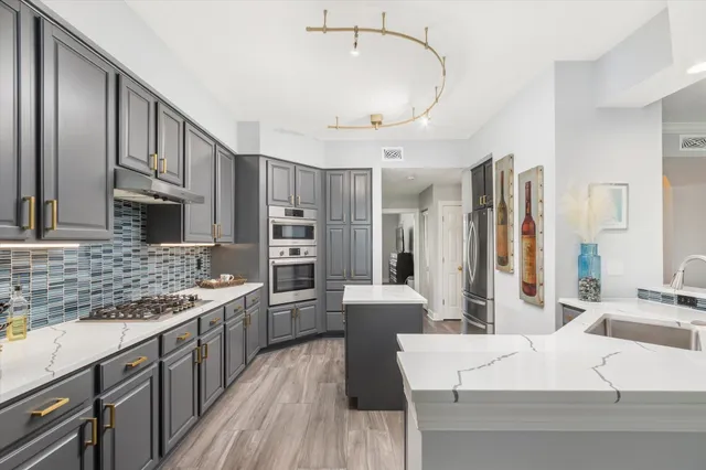 a large white kitchen with stainless steel appliances kitchen island granite countertop a large stove a sink dishwasher and white cabinets with wooden floor