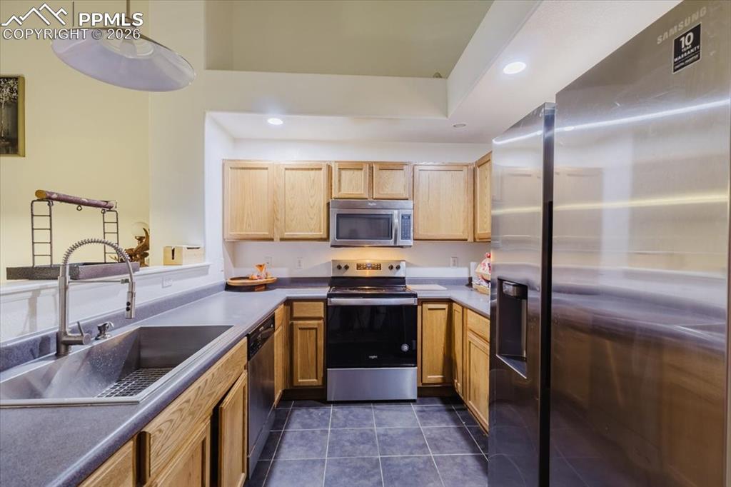 5800 Tower Road, Unit 108 Denver, CO 80249 - Photo 19 of 35 U-shaped kitchen featuring light wood cabinetry, stone-finish countertops, stainless steel appliances, and dark tile flooring