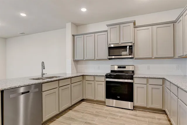 a kitchen with granite countertop a sink a stove a microwave a refrigerator and white cabinets