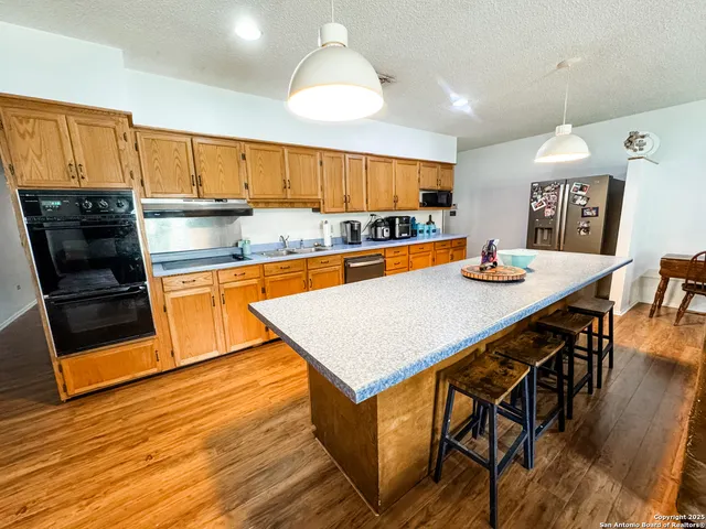 a kitchen with stainless steel appliances granite countertop a kitchen island a stove a sink a dining table and chairs with wooden floor