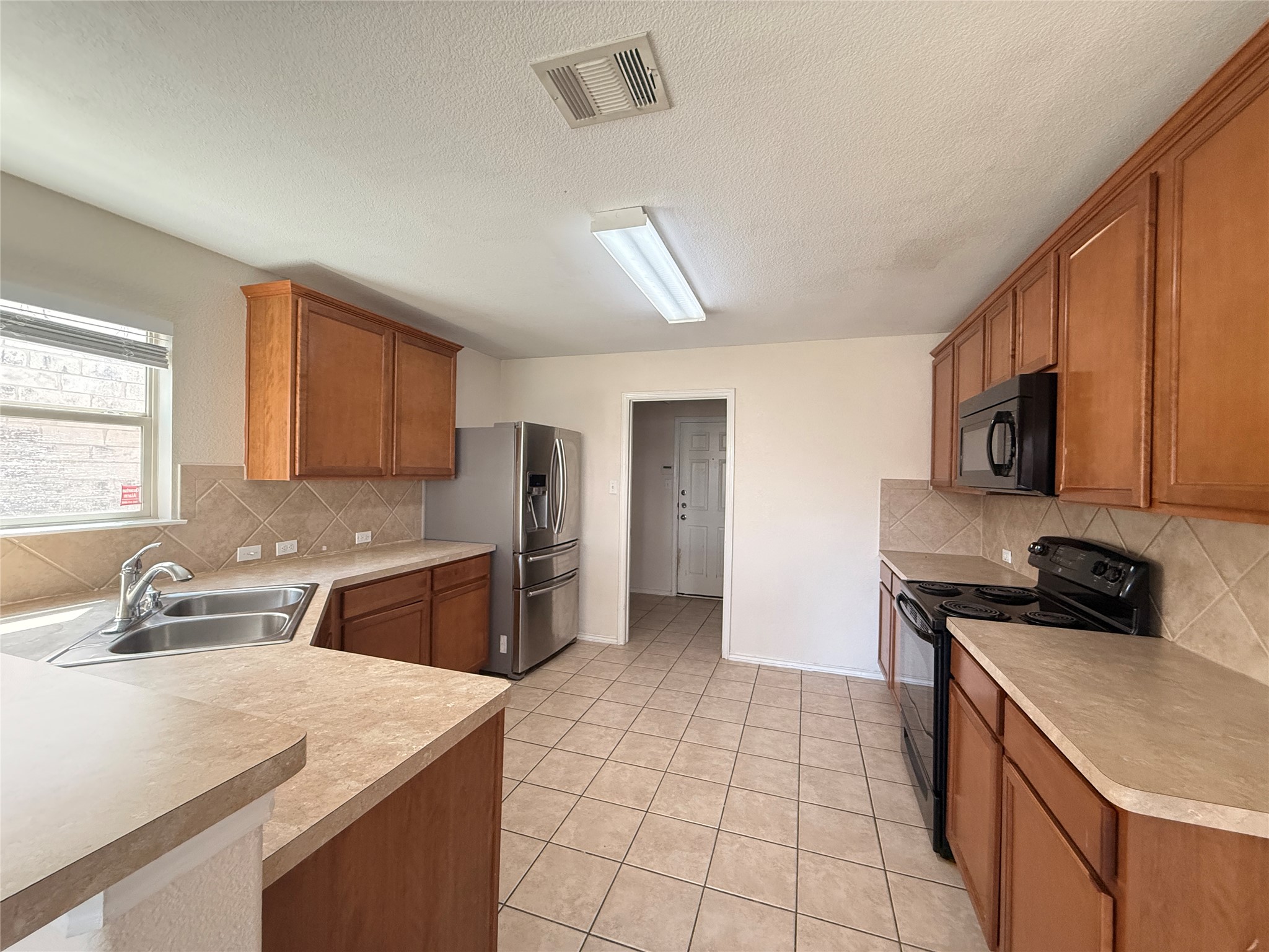279 Housefinch Loop Leander, TX 78641 - Photo 11 of 30 Kitchen with wood finish cabinetry, black appliances, decorative backsplash, light countertops, and a textured ceiling